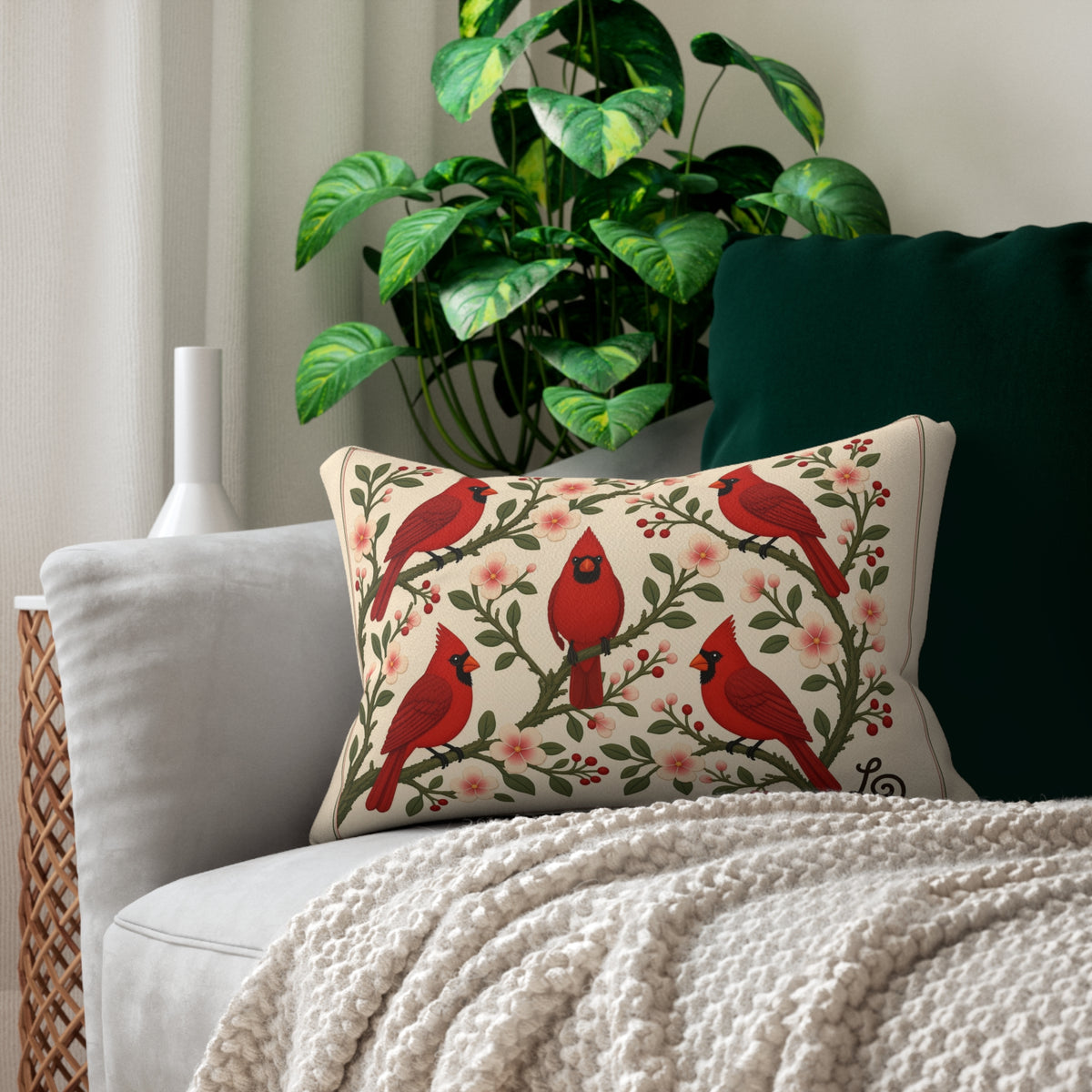 Winter Cardinals & Blossoms lumbar pillow by LQ styled on a sofa with a textured throw beside a leafy plant